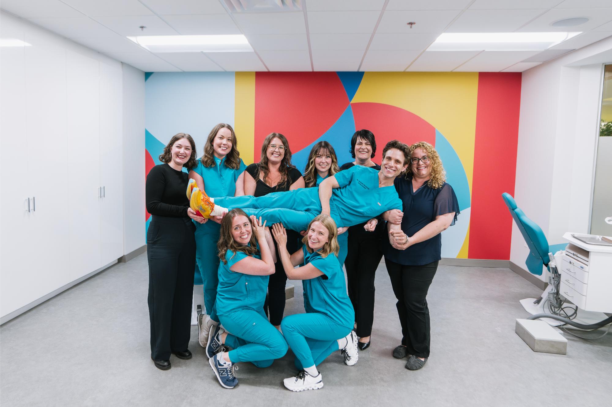 Paradigm-Team-2025-01111 Team of orthodontic professionals at Paradigm Orthodontics in Halifax, featuring Dr. Emanuele, smiling and posing in a colorful clinic setting, showcasing a welcoming atmosphere for patients.