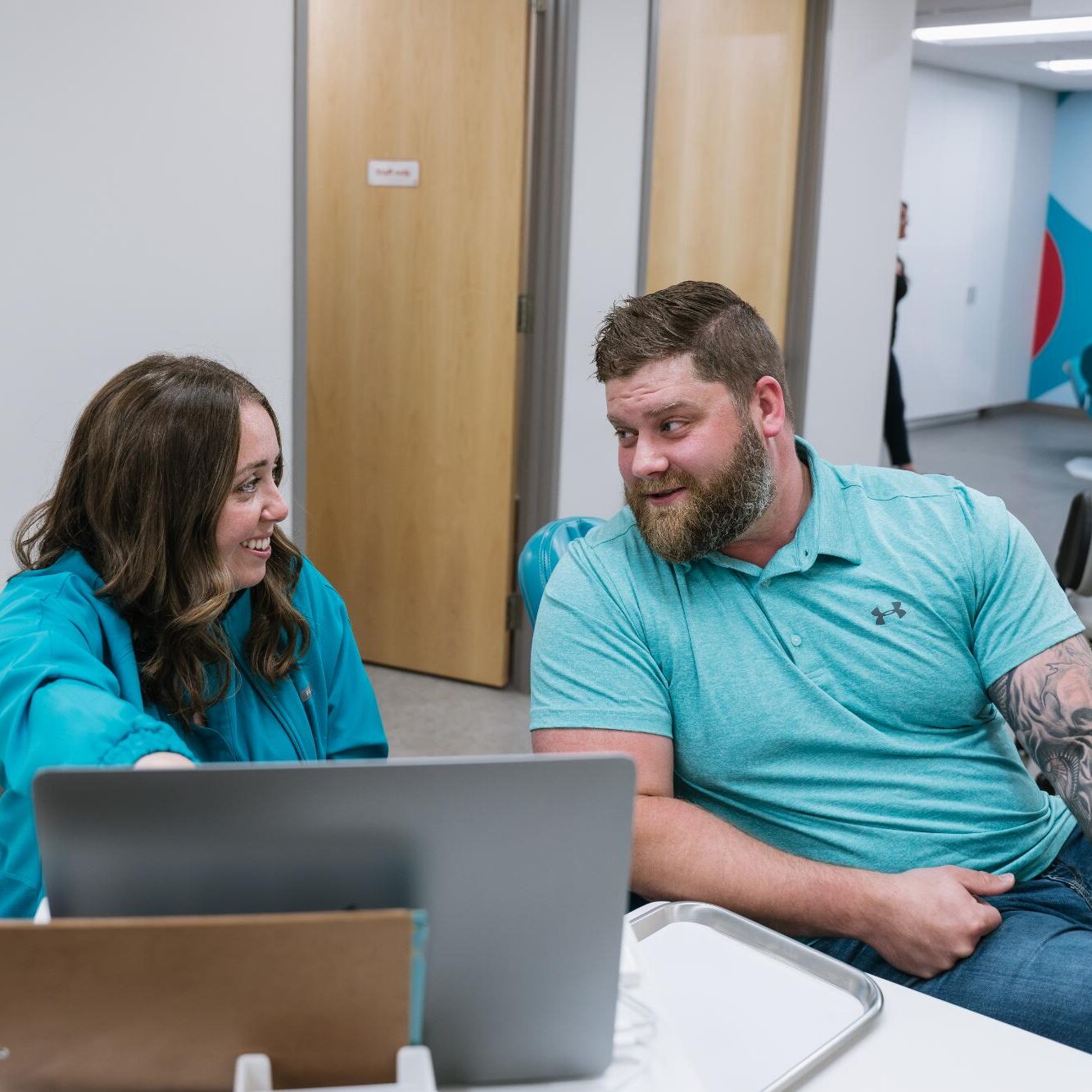 Patient consulting with orthodontist in modern clinic setting, discussing clear braces options with a laptop visible.