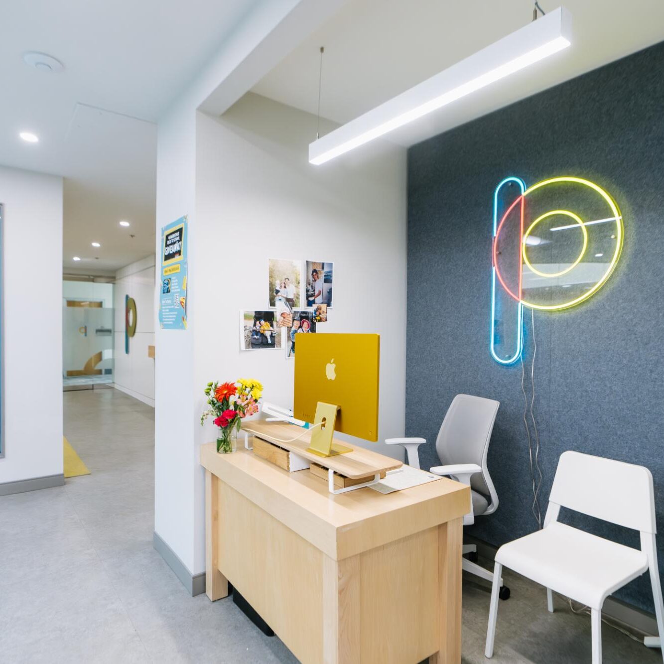 Modern orthodontic office reception area at Paradigm Orthodontics in Halifax, featuring a sleek wooden desk, yellow Apple computer, vibrant neon signage, and floral arrangement, emphasizing a clean and welcoming environment.