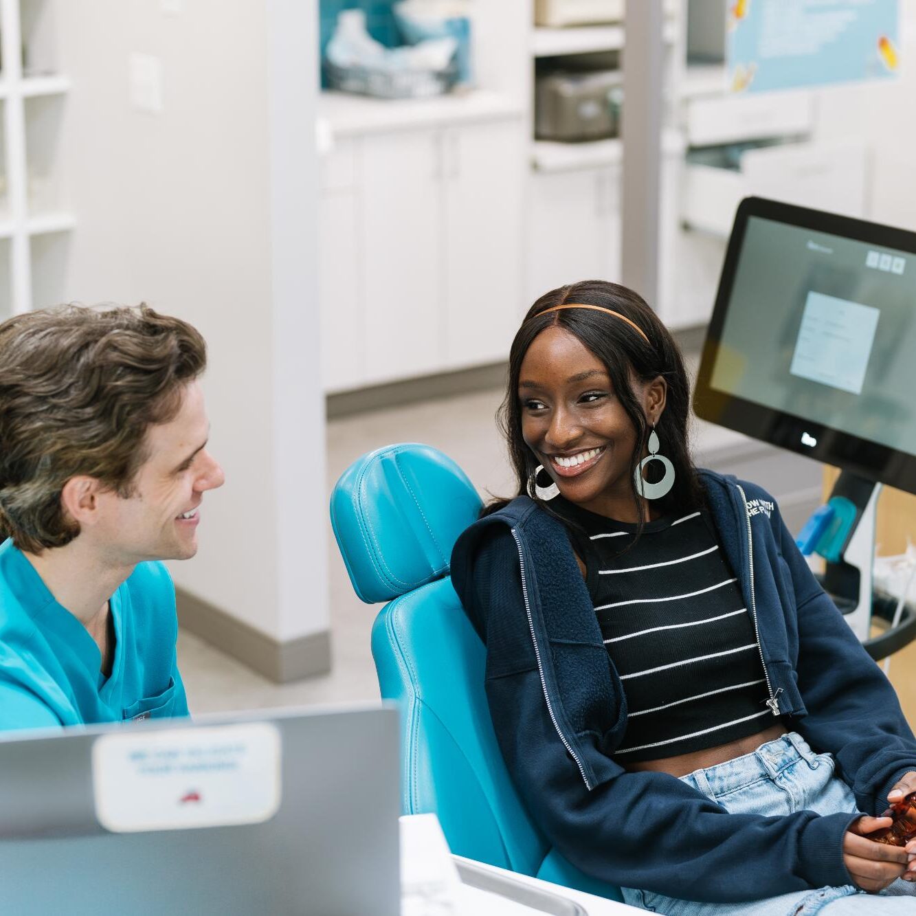 Paradigm-2025-09838 Smiling patient in dental chair interacting with orthodontist in modern clinic, discussing Invisalign treatment options at Paradigm Orthodontics.